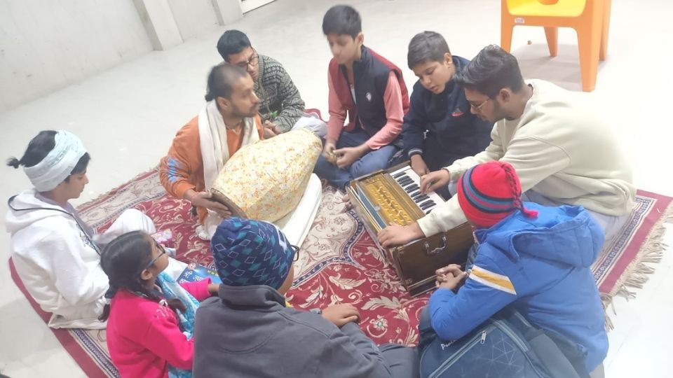Children learning traditional harmonium and mridanga rhythms with devotee mentors